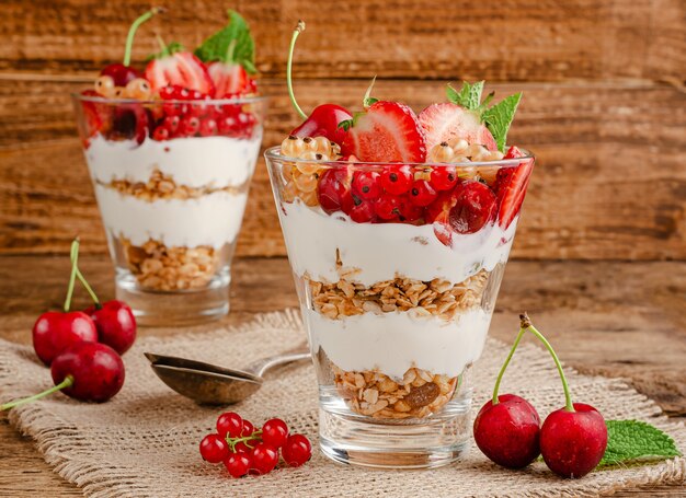 Jars of granola with yogurt and red berries on wooden rustic wall.