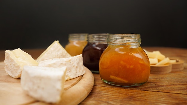 ガラスの瓶に入った自家製ジャムと蜂蜜の瓶と木製のテーブルの上のさまざまなチーズ前菜用のチーズプレート選択的な焦点