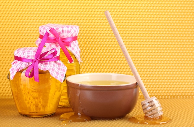 Jars of honey bowl and wooden drizzler with honey on yellow honeycomb background