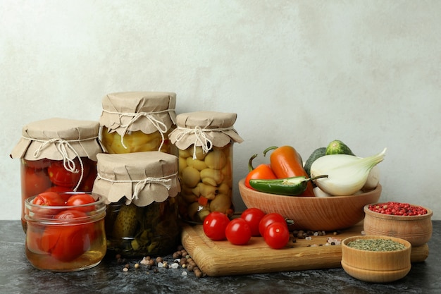 Jars of pickled vegetables and ingredients on black smokey table