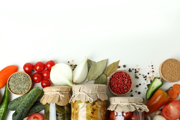 Jars of pickled vegetables and ingredients on white table