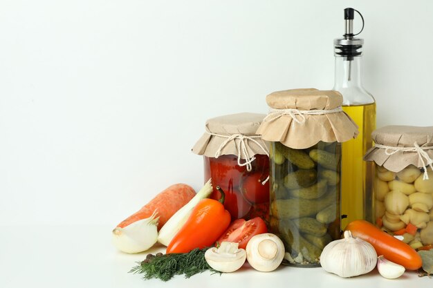 Jars of pickled vegetables and ingredients on white table