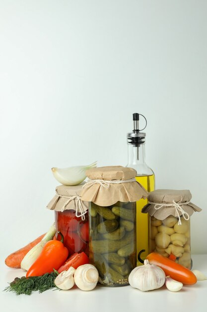 Jars of pickled vegetables and ingredients on white table