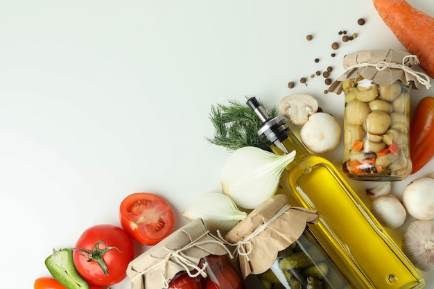 Jars of pickled vegetables and ingredients on white table