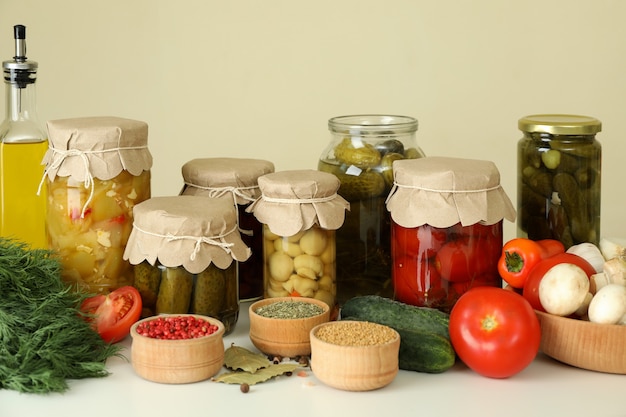 Jars of pickled vegetables and ingredients on white table