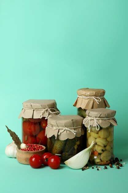 Jars of pickled vegetables on mint background