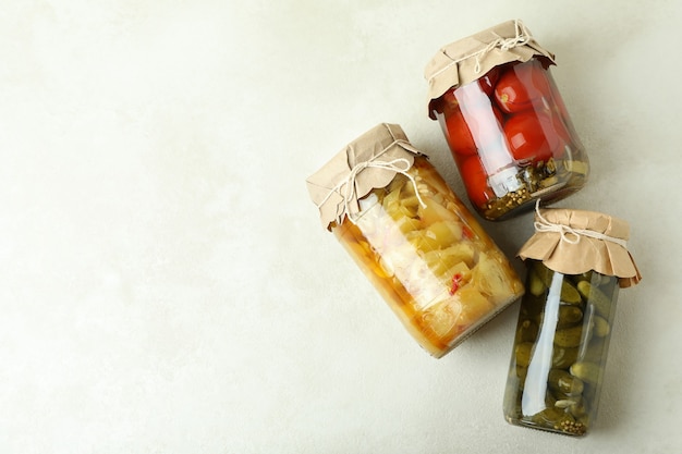 Jars of pickled vegetables on white textured background