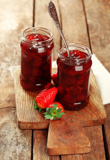 Jars of strawberry jam with berries on wooden background