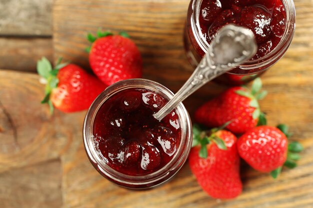 Photo jars of strawberry jam with berries on wooden background