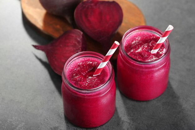 Jars with beetroot smoothie and fresh vegetables on grey background