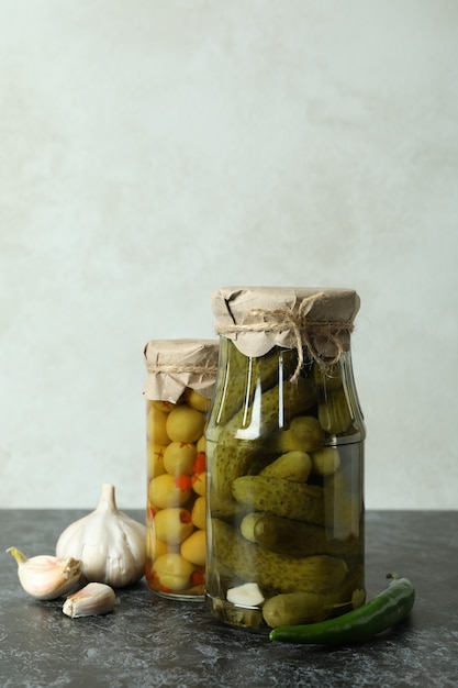 Jars with canned cucumbers and olives on black smokey table