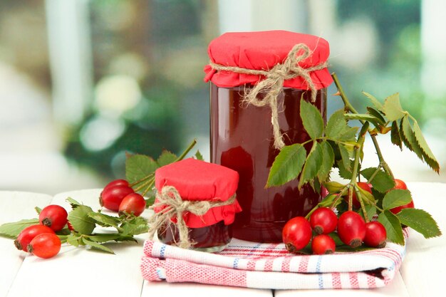 Jars with hip roses jam and ripe berries on wooden table