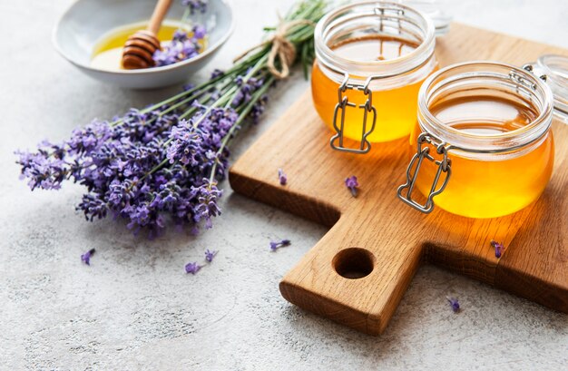 Jars with honey and fresh lavender flowers on a concrete background
