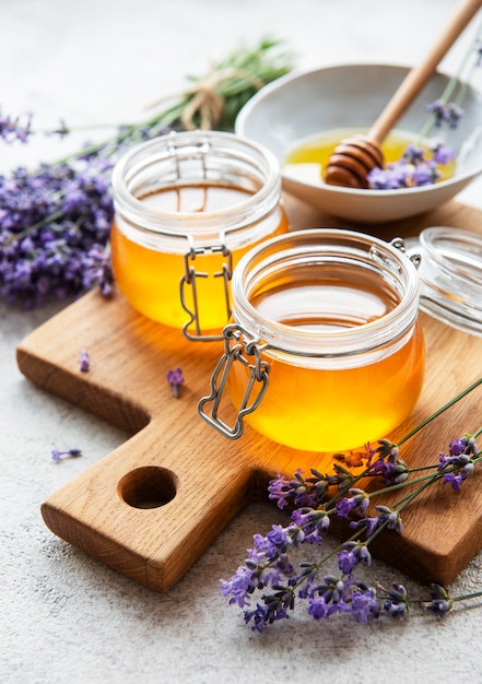 Jars with honey and fresh lavender flowers on a concrete background