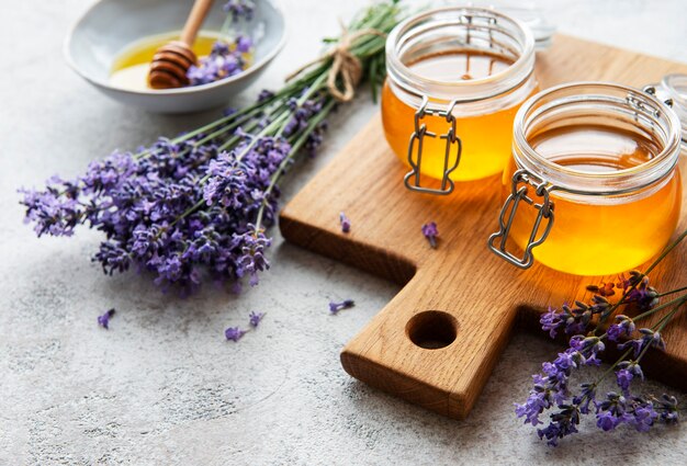 Jars with honey and fresh lavender flowers on a concrete background