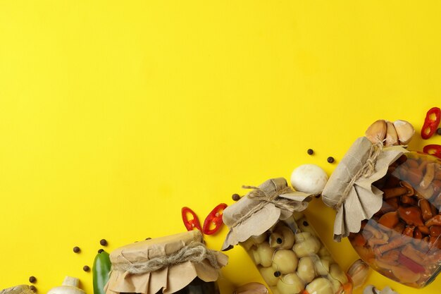 Jars with marinated mushrooms on yellow background