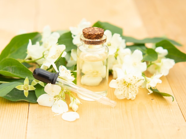 Jasmine essential oil in a glass bottle on a background of jasmine flowers on a wooden table