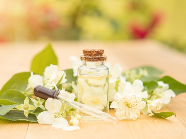 Jasmine essential oil in a glass bottle on a background of jasmine flowers on a wooden table