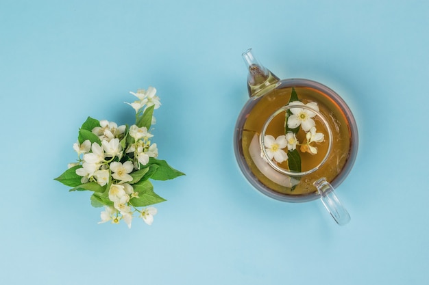 Jasmine flowers and a teapot with jasmine tea on a blue
background.