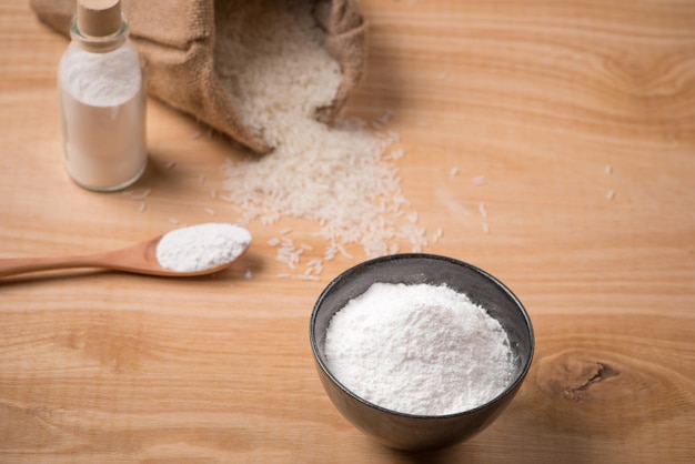 Jasmine white rice in sack and rice flour on wooden table.