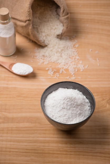 Jasmine white rice in sack and rice flour on wooden table.