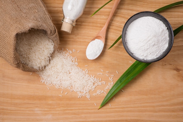 Jasmine white rice in sack and rice flour on wooden table.