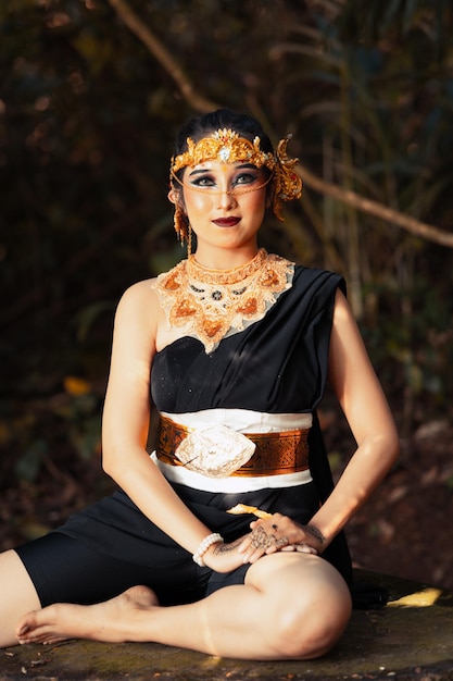 Javanese woman with golden crown and black costume chilling inside the forest while wearing makeup