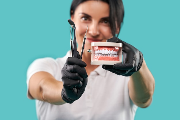 Jaw cast and dental tools in the hands of a young beautiful blurred dentist woman isolated on a blue background. Carver, extractor and dental mirror.