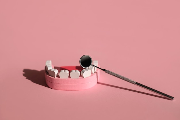 Фото Модель челюсти и стоматологическое зеркало на розовом фоне стоматолог и день гигиены полости рта