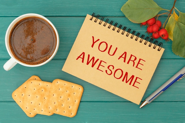 Foto je bent geweldig - een inscriptie op een notitieboekje, warme koffie en koekjes op een houten tafel