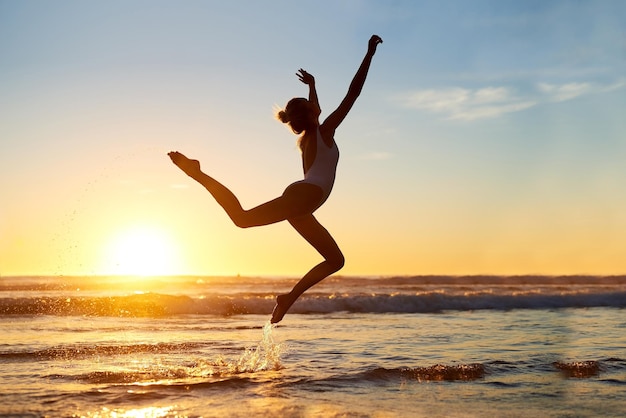 Je bent vrij om te zijn wie je ook bent Shot van een jonge vrouw die midden in de lucht springt tegen een prachtige zonsondergang op het strand