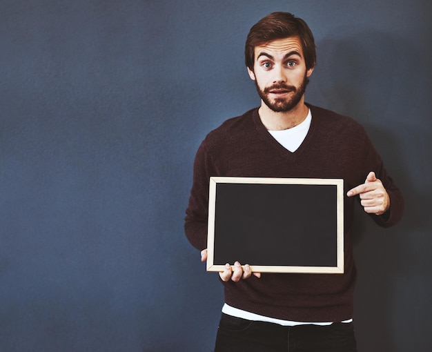 Je bericht zou hier indruk maken studioportret van een jonge man die naar een schoolbord wijst tegen een grijze achtergrond