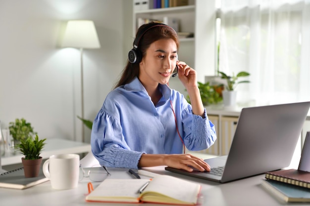 Je goed, gelukkig en positief voelen op het werk. Jonge Aziatische onderneemster die hoofdtelefoon op videogesprek met cliënten op laptop draagt. Jonge Aziatische vrouw die online educatieve klassenlezing geeft, klant raadpleegt.