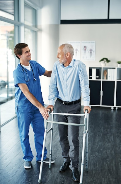 Je hebt een grote verbetering gemaakt. Foto van een verpleger die een oudere patiënt met een rollator helpt