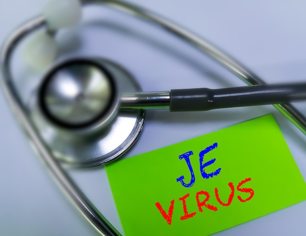 JE virus medical term word in green card on white background with stethoscope. Japanese encephalitis