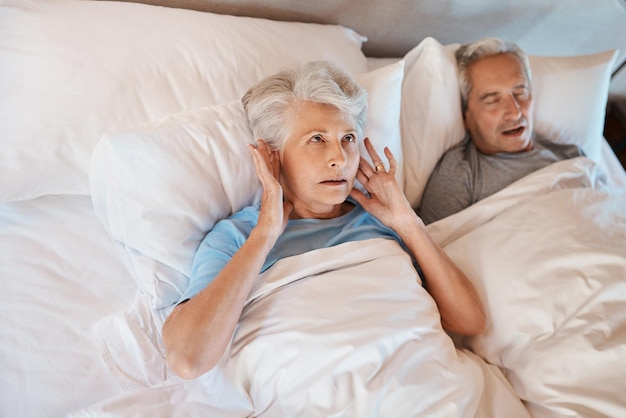 Foto je zou denken dat ik aan zijn snurken gewend zou zijn bijgesneden opname van een oudere vrouw die gefrustreerd haar oren blokkeert terwijl haar man in bed naast haar snurkt