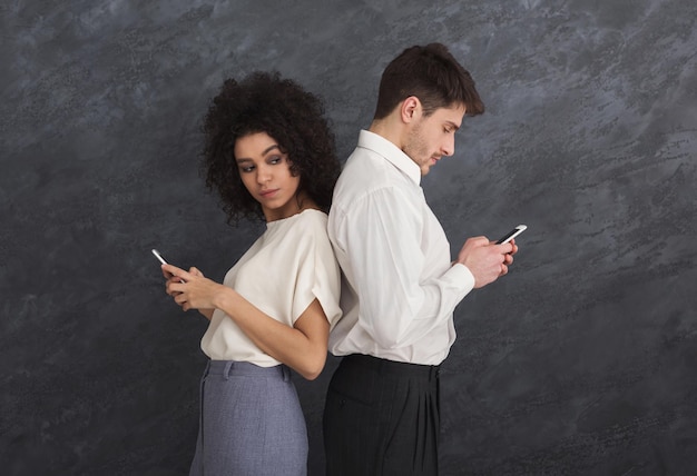 Jealous girlfriend watching her boyfriend texting on phone, social network addiction concept, gray studio background, copy space