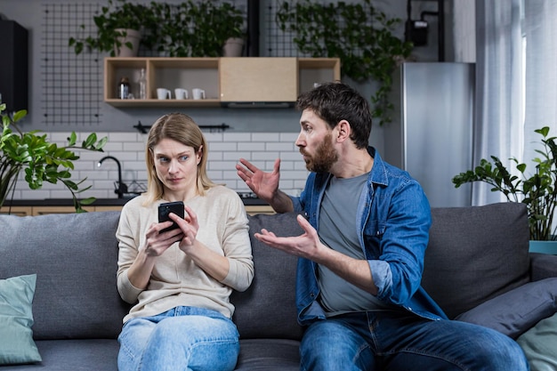 jealous man shouting at woman over the phone married couple quarreling at home sitting on sofa