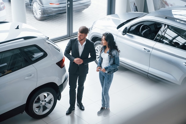 In jeans and white shirt. Female customer and modern stylish bearded businessman in the automobile saloon.