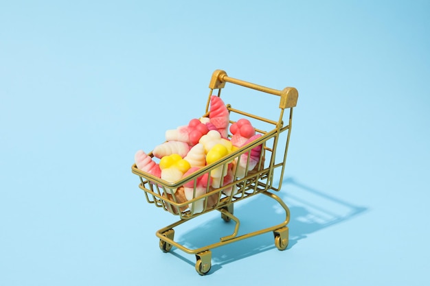 Jelly candies in shopping trolley on blue background