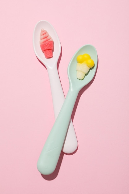 Jelly candies in spoons on pink background top view