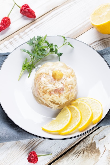 Jelly on a plate with lemon slices, parsley and mustard. Chili pepper is on the table.