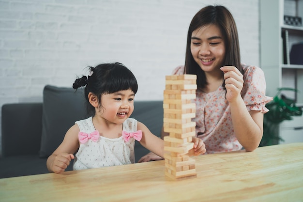 Jenga-spellenconcept Aziatische dochter en moeder die gelukkig glimlachen en lachen met het spelen van houten jenga-spellen zittend op de bank in de woonkamer thuis moeder en dochter familieactiviteiten die gelukkige spellen spelen