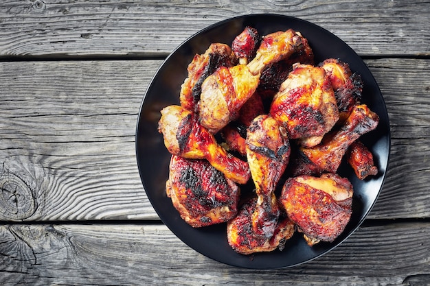 Jerk Chicken on a black plate on a rustic wooden table, horizontal view from above, close-up, flatlay, copy space