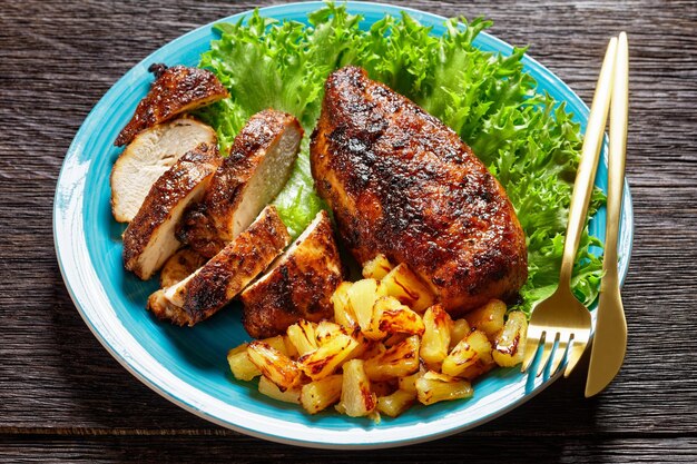 Jerk chicken borsten met gegrilde ananasblokjes en verse groene blaadjes sla op een blauw bord op een houten tafel