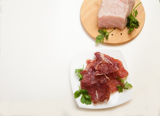 Jerky in a cup and raw meat with herbs on a white plate. Copy spaes.