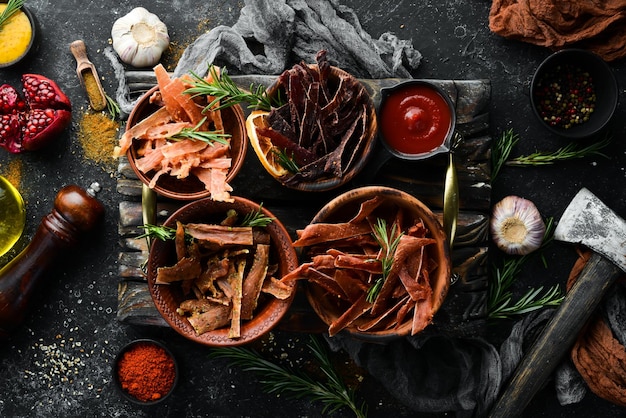 Jerky Dried meat slices with spices and herbs Snacks for beer On a black stone background Top view