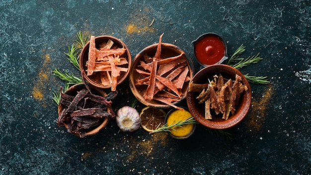 Jerky Dried meat slices with spices and herbs Snacks for beer On a black stone background Top view