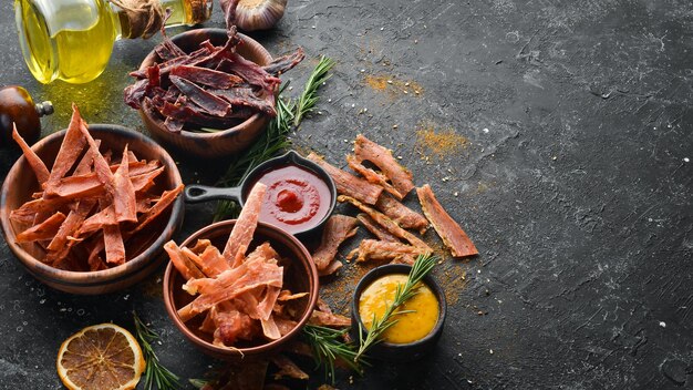 Jerky Dried meat slices with spices and herbs Snacks for beer On a black stone background Top view