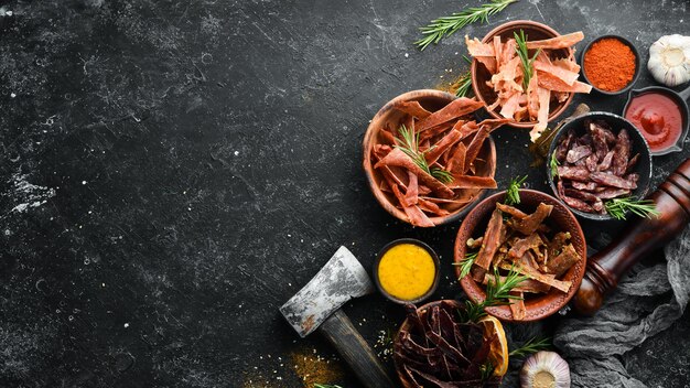 Jerky Dried meat slices with spices and herbs Snacks for beer On a black stone background Top view